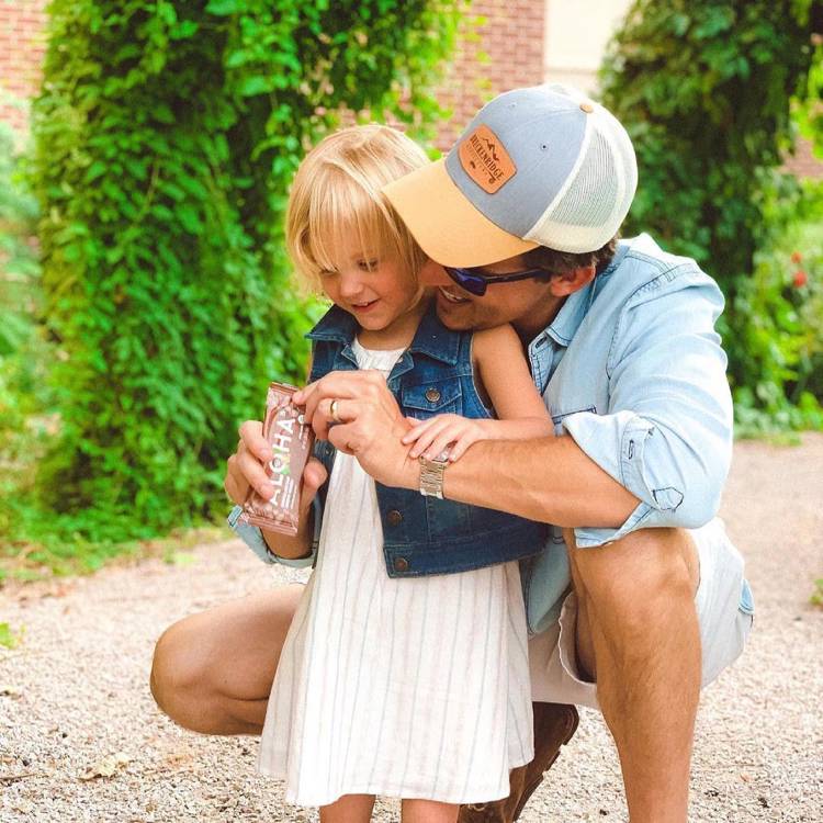 a man is kneeling down next to a little girl and holding a snack