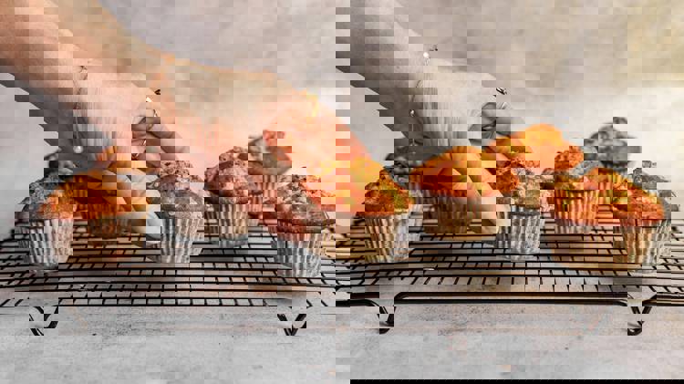 a woman reaches for a cupcake on a cooling rack