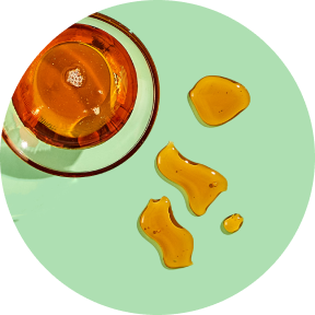 Glass of amber liquid with droplets on a green surface.