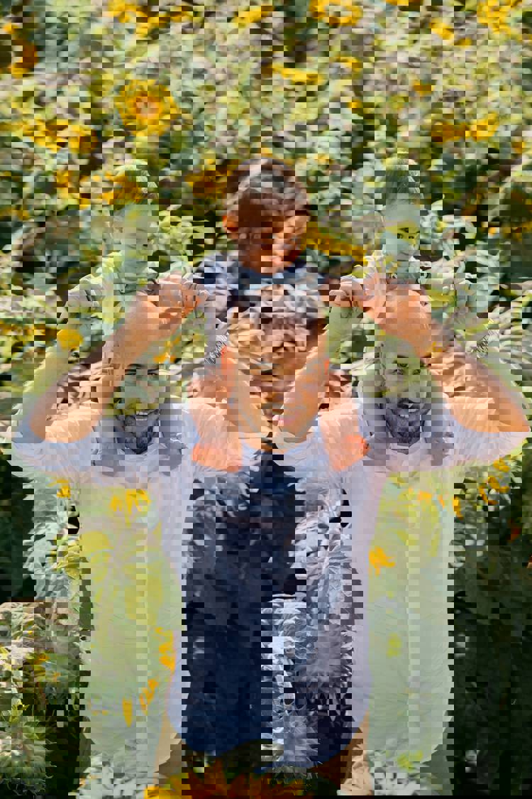 a man is carrying a baby on his shoulders in a field of sunflowers